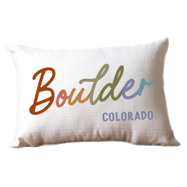 White rectangular pillow with 'Boulder Colorado' text in multicolor gradient script on textured fabric.